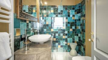 A bathroom with a white sink, a glass bowl, a modern shower, and a toilet.