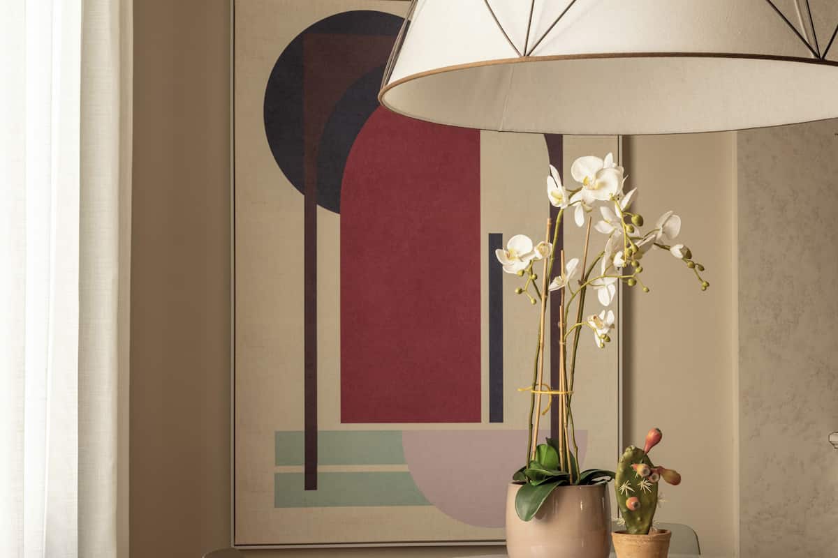 A dining area with a round table, two chairs, a potted orchid, a cactus, and a modern abstract painting on the wall.