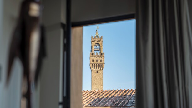 A view of a historic tower through a window, with a clear sky visible. - Canto degli Scali (Florence)