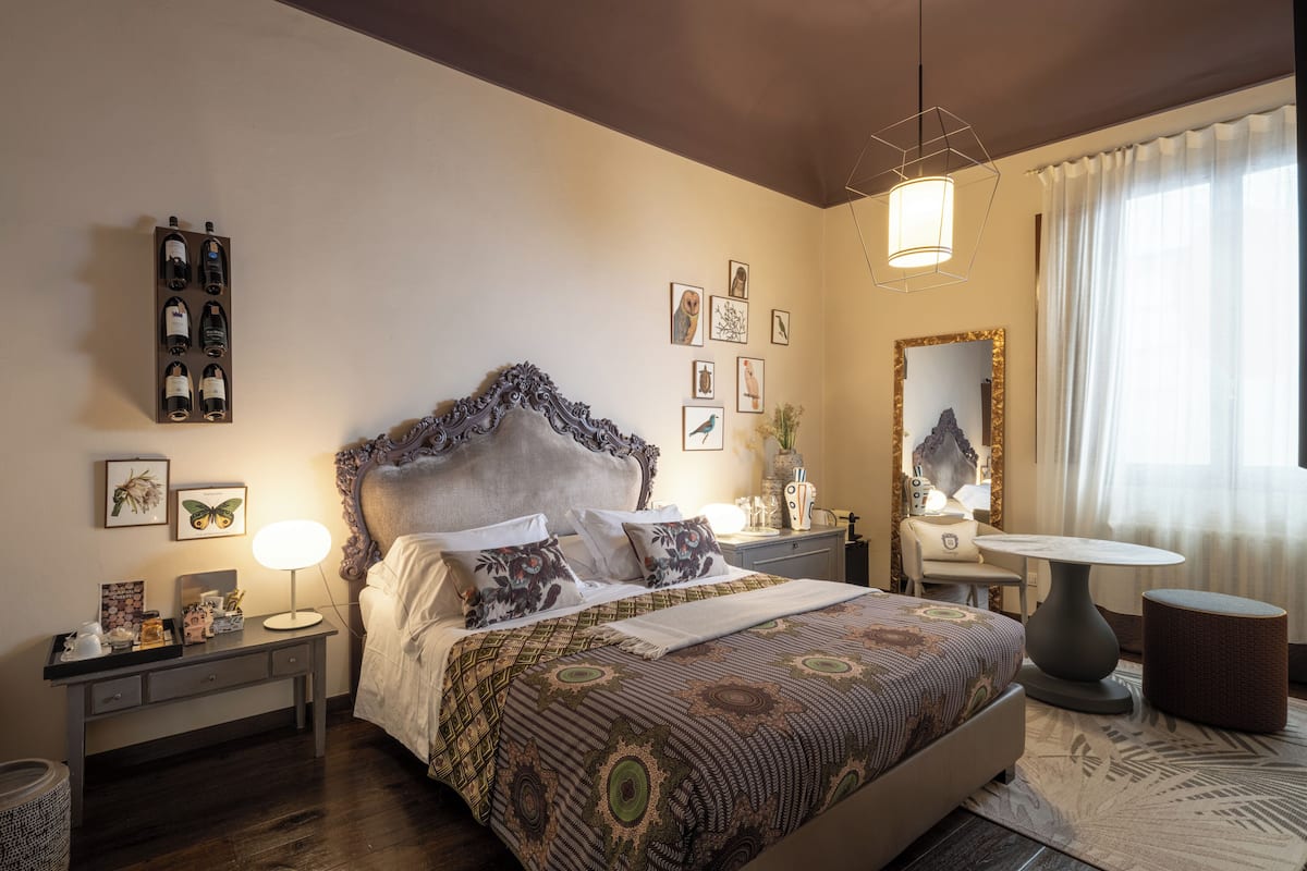 A well-appointed bedroom with a large bed, a bedside table with a lamp, a small round table, and a mirror.