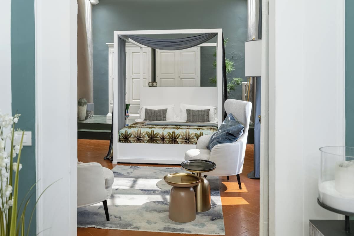 A bedroom with a canopy bed, a white armchair, a small round table, and a glass display case.
