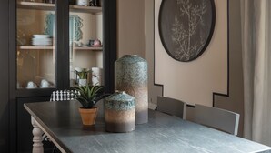 A dining area with a dark wooden table, two potted plants, and a large vase. A coffee maker and glassware are visible on shelves behind the table. - Canto degli Scali (Florence)