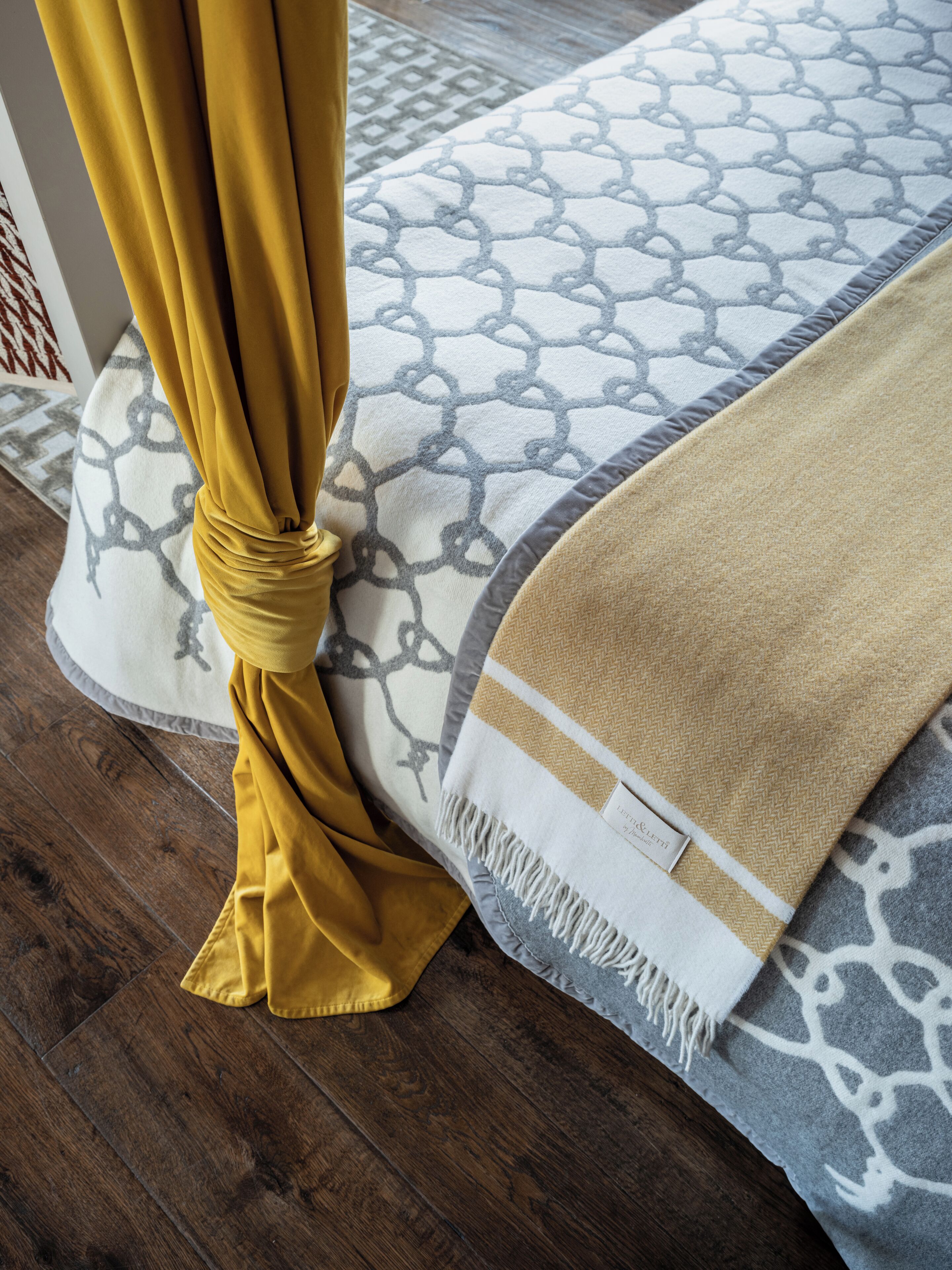 A bed with patterned bedding and a yellow curtain.
