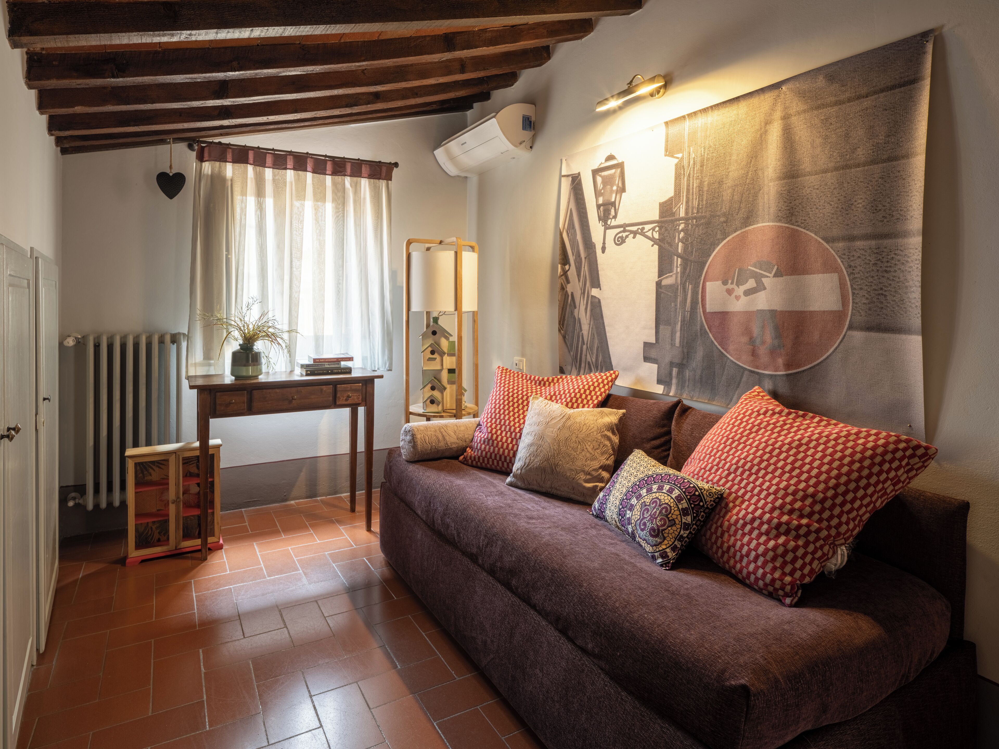 A cozy living room with a brown sofa, patterned cushions, a wooden coffee table, a radiator, and a large wall mural.