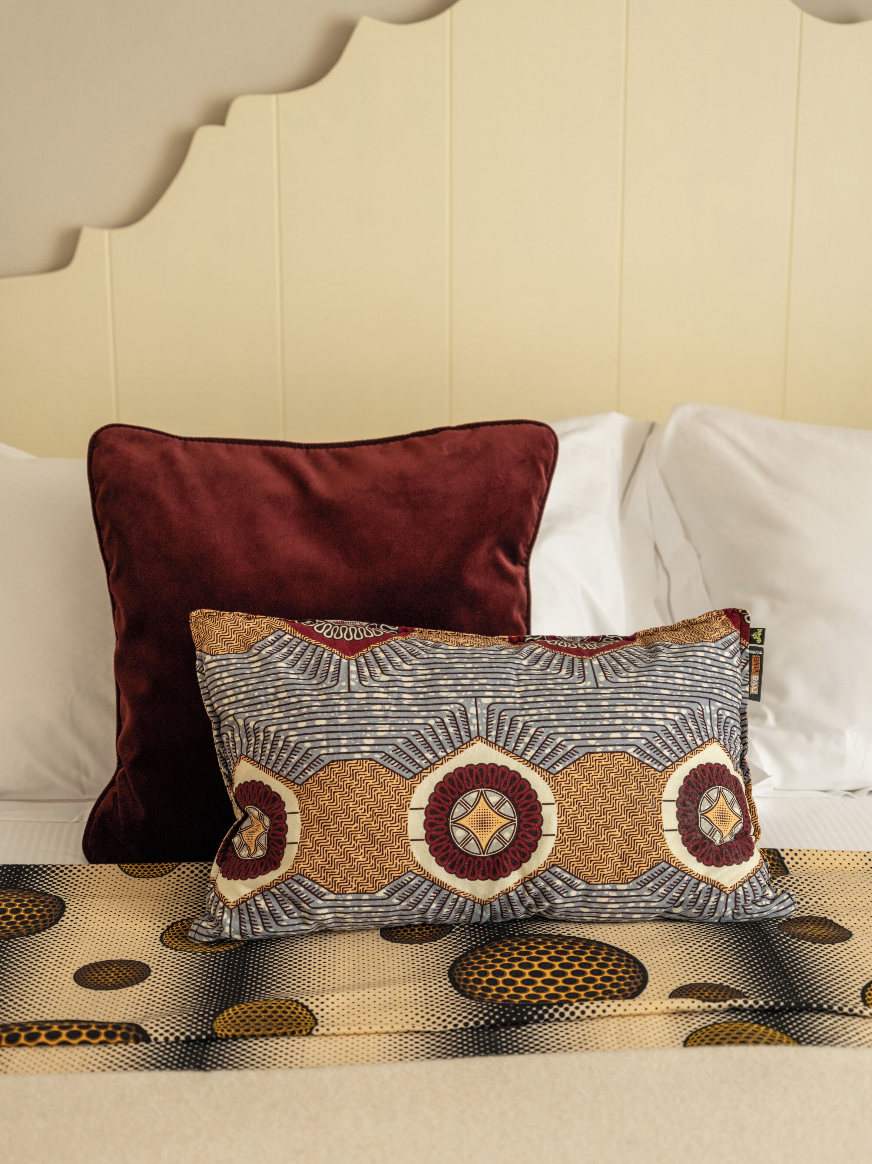 Una cama con dos almohadas, una roja y otra con diseños geométricos.