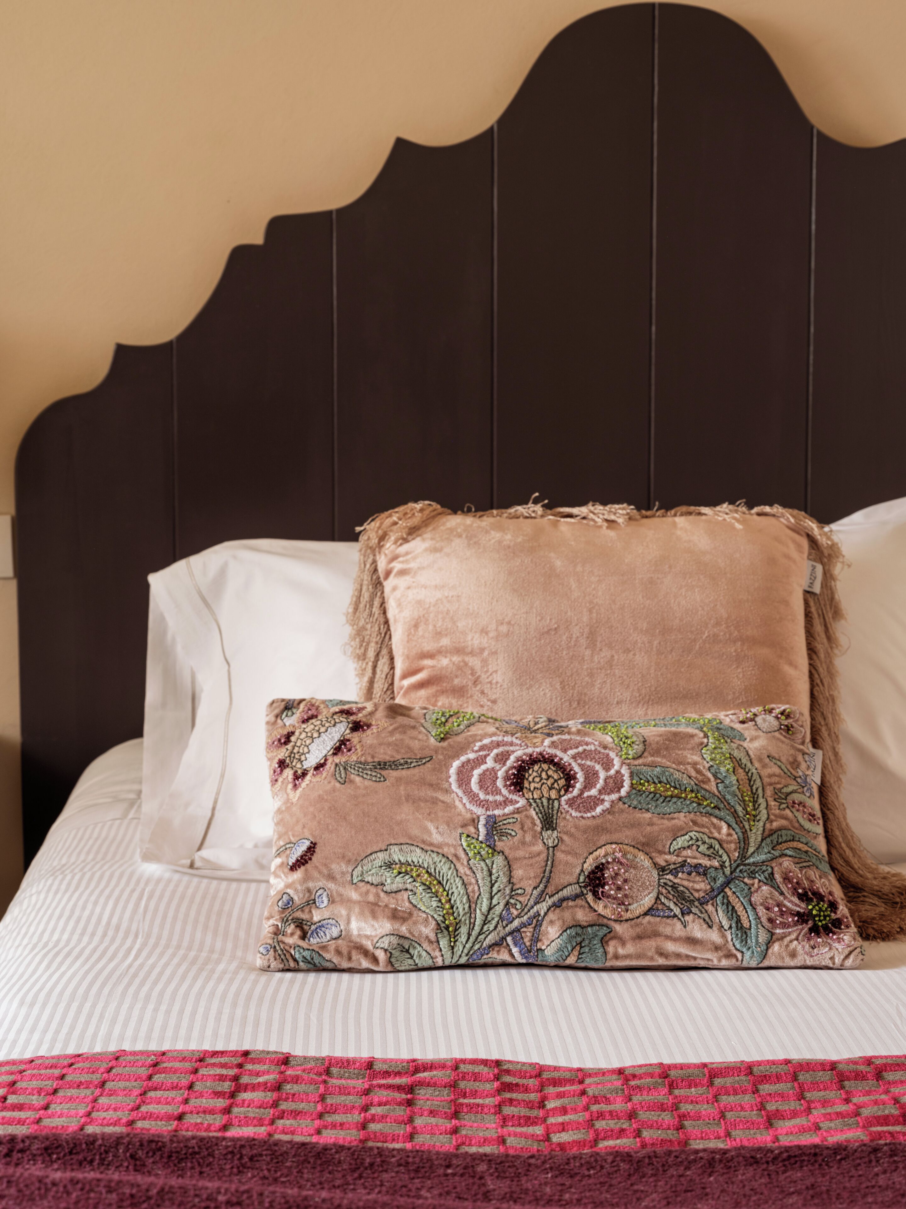 Un lit avec une tête de lit sombre, un coussin à motifs floraux et une couverture rouge et beige.