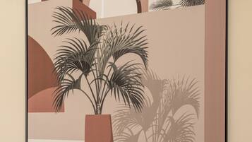 A framed artwork depicting a potted plant with palm fronds in a geometric setting.