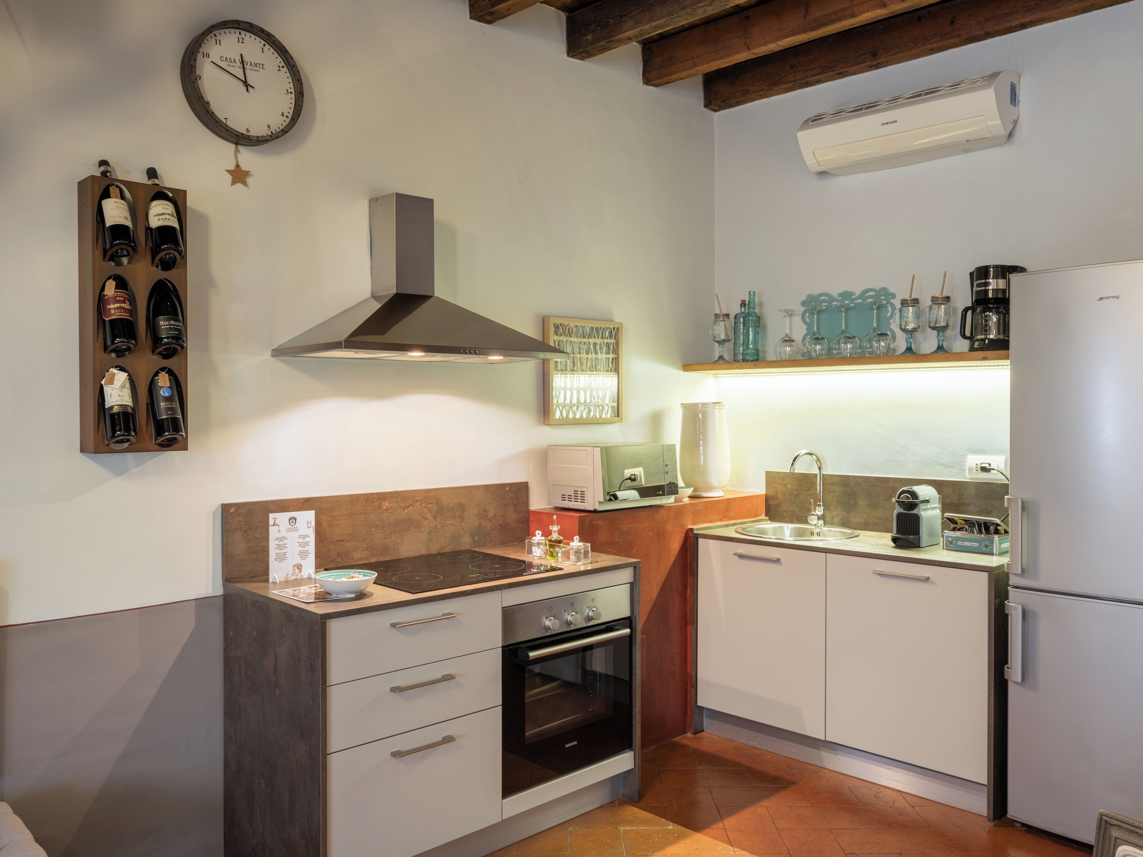 A modern kitchen with a built-in oven, a stove, and a sink. There is a wine rack on the wall and a clock above it.