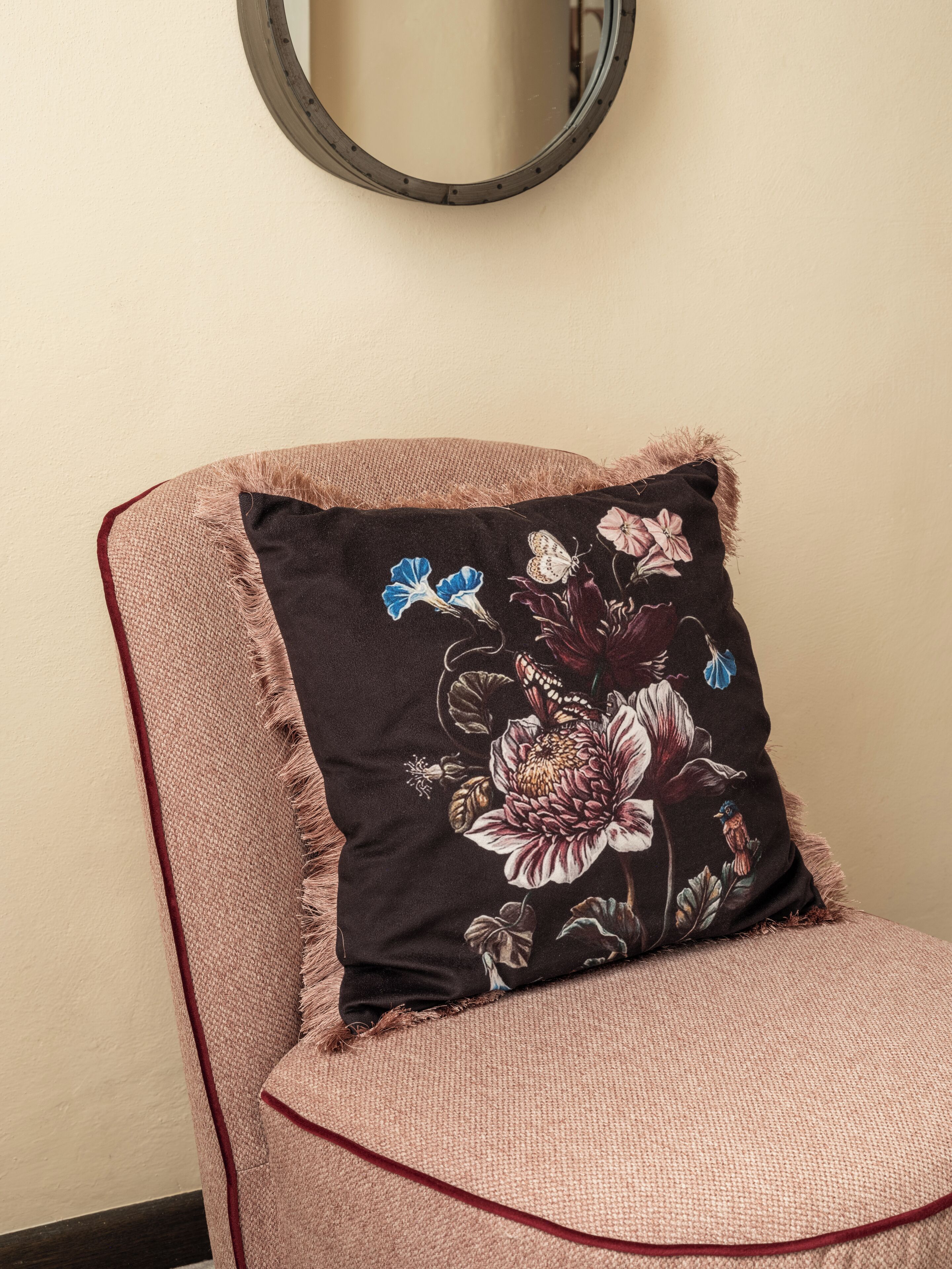 A chair with a floral pillow and a round mirror on the wall.