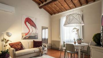 A living room with a sofa, a coffee table, a dining table with chairs, a hanging light fixture, and a radiator.