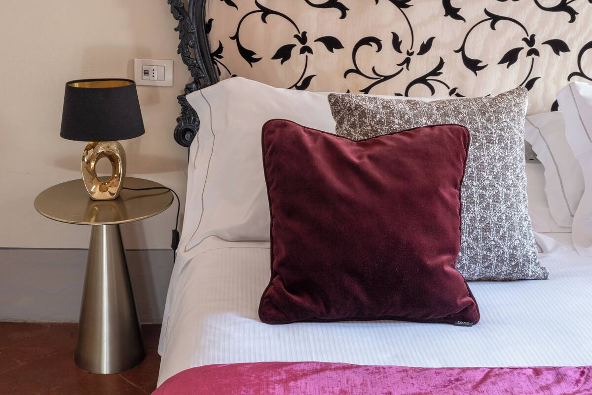 A neatly made bed with a patterned headboard, a bedside table with a lamp, and a decorative pillow.