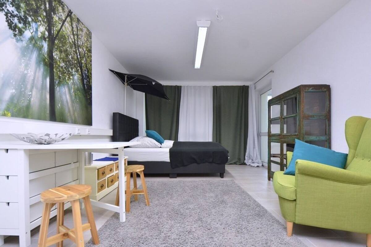 Une chambre moderne avec un lit, un bureau, un fauteuil vert et une bibliothèque.