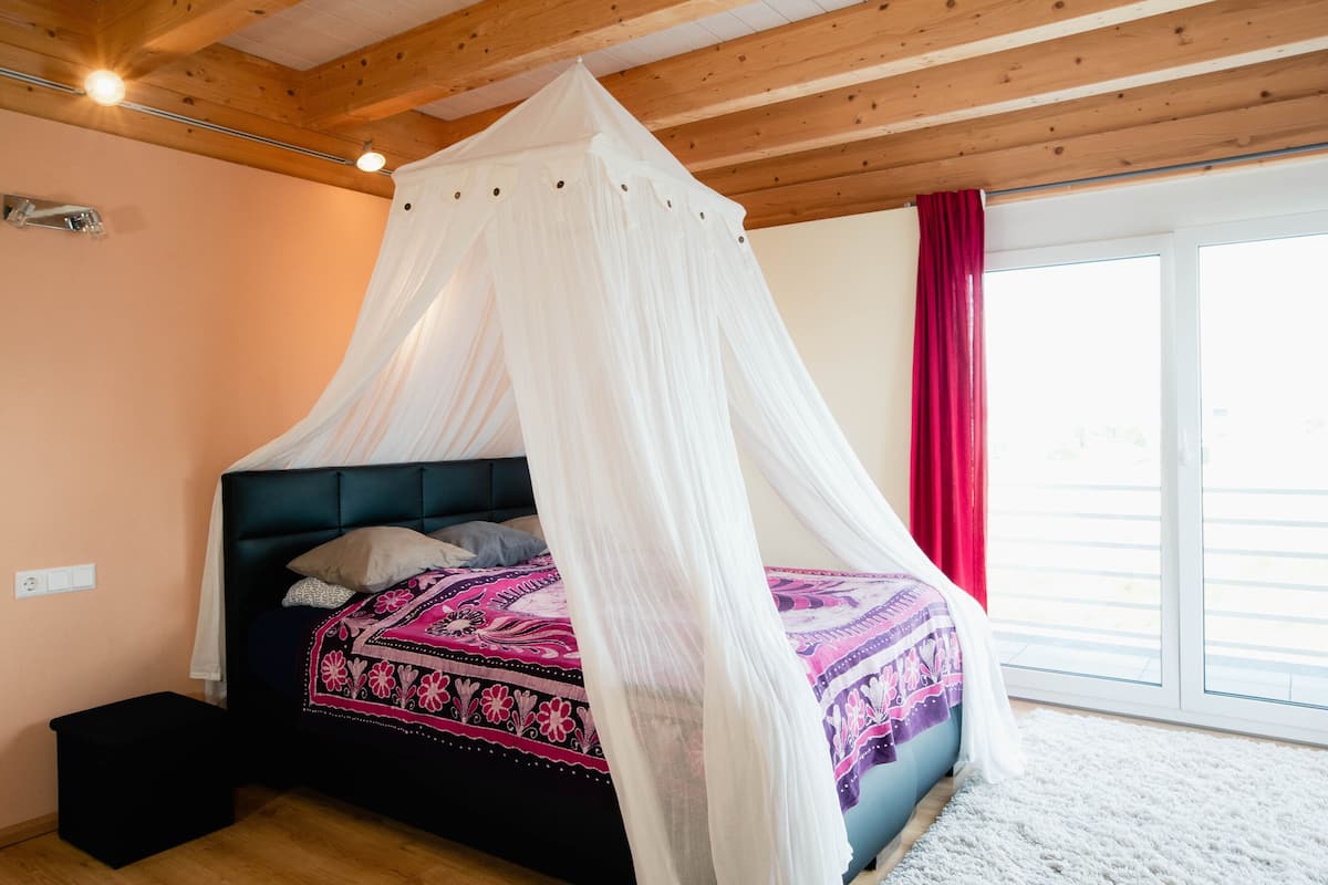 Une chambre à coucher avec un lit sous un dais, une fenêtre avec des rideaux rouges et un plafond en bois.