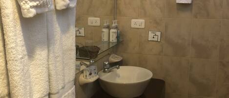 Une salle de bain avec des toilettes blanches, un lavabo surmonté d’un miroir et un porte-serviettes avec des serviettes blanches.