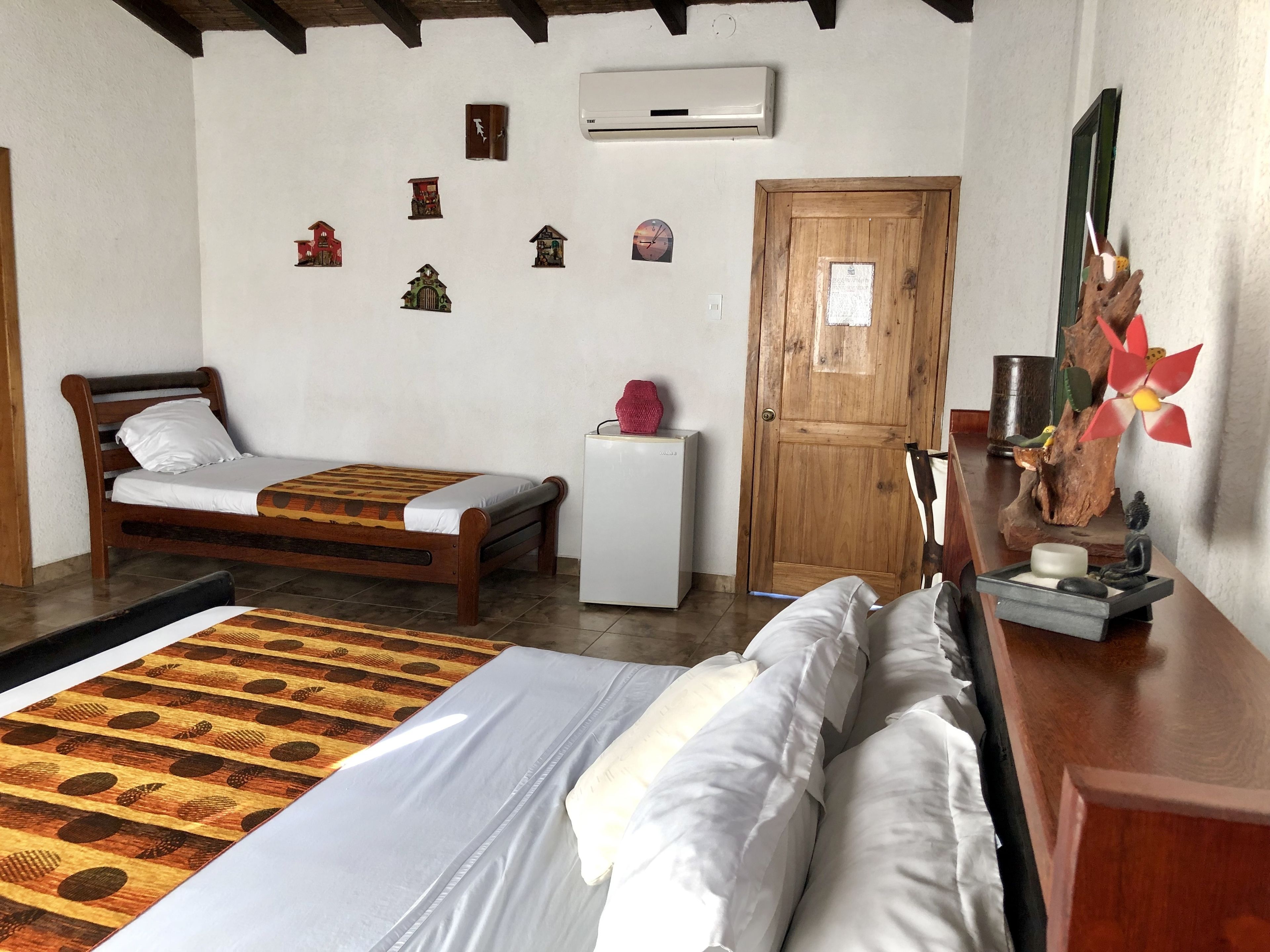 Una habitación con cama, una mesita de noche, una puerta de madera y un aire acondicionado de pared.