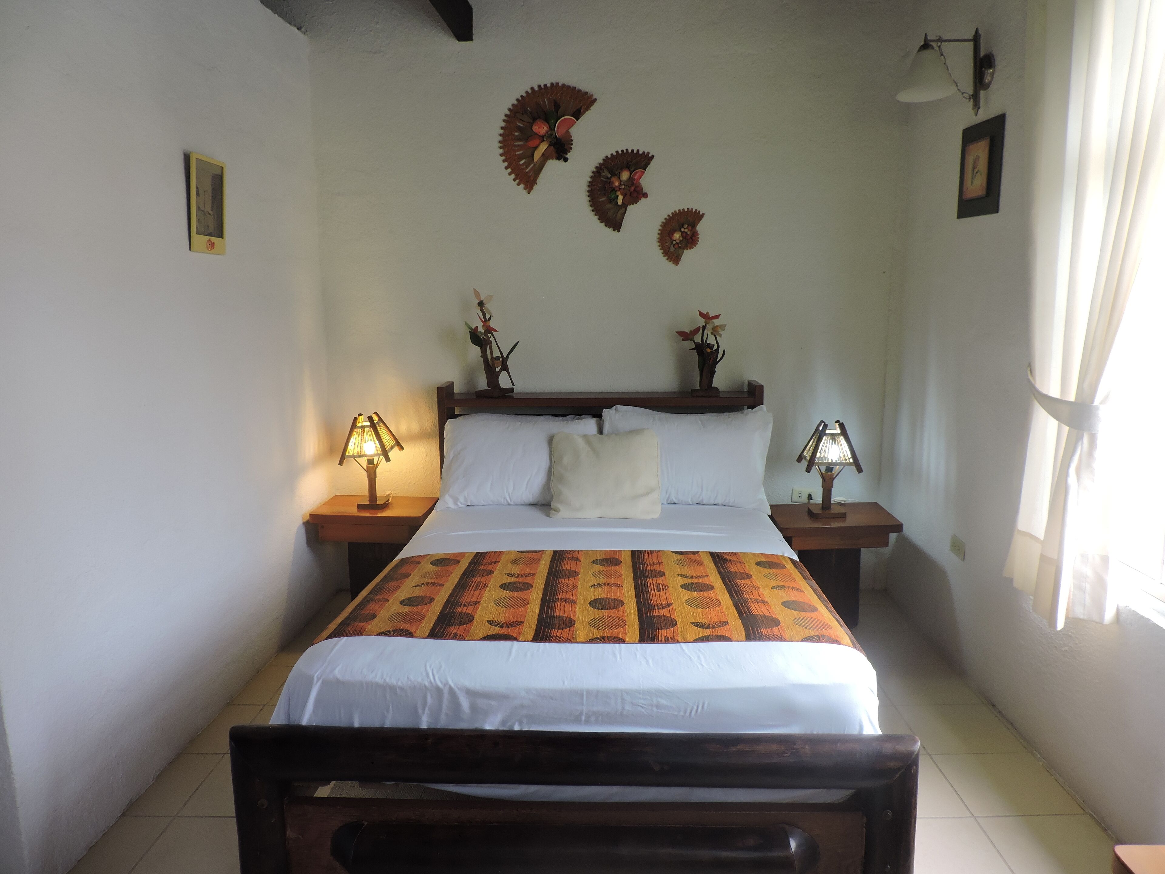 A neatly made bed with a patterned bedspread, two bedside lamps, and wall-mounted decorative items.