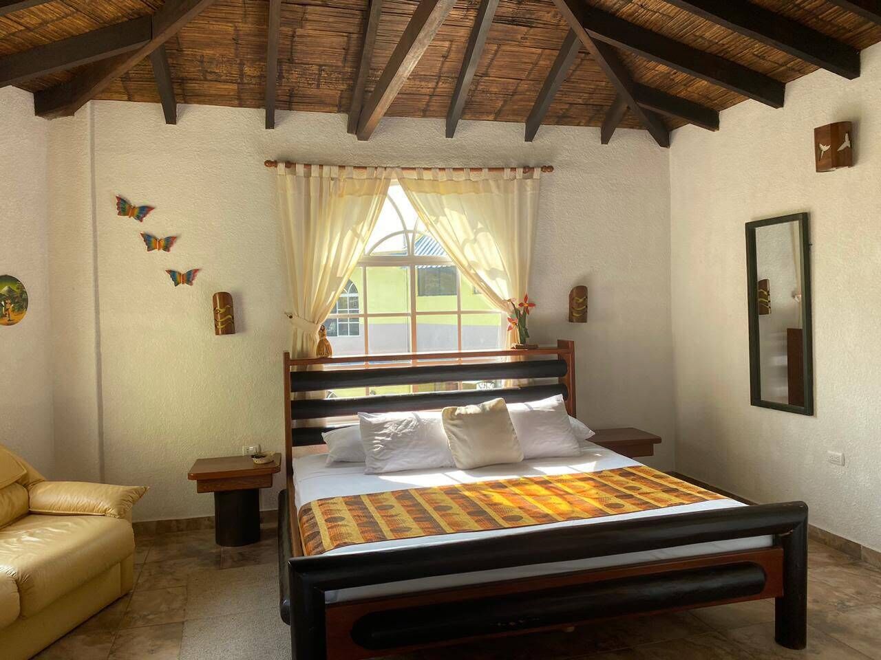 Un dormitorio con una cama, una silla, una mesita de noche, una ventana con cortinas y un espejo en la pared.