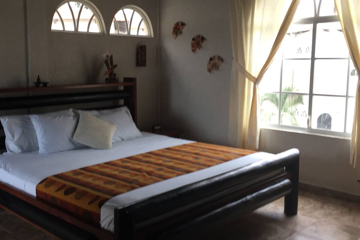 Un dormitorio con cama de madera, ropa de cama blanca y ventana con cortinas.