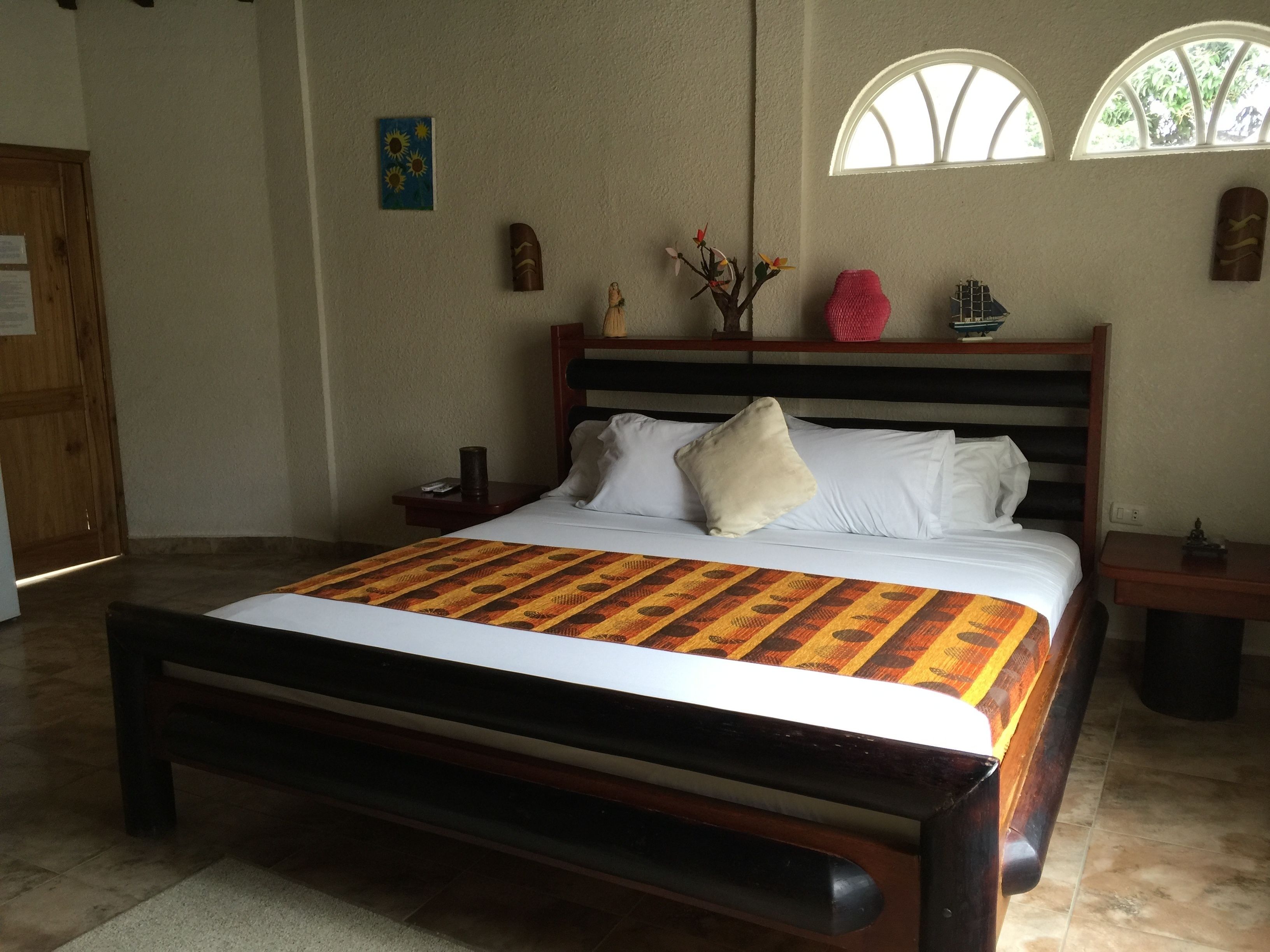 Una cama bien tendida con una colcha estampada, un cabecero de madera y una mesita de noche con una lámpara.