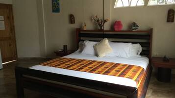 Una cama bien tendida con una colcha estampada, un cabecero de madera y una mesita de noche con una lámpara.
