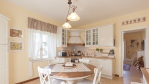 A well-lit kitchen with white cabinets, a dining table with chairs, and a hanging light fixture. - Nina Guest House (Castegnero)