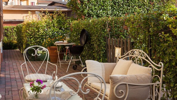 A patio with a white metal chair, a small table with a vase of flowers, and a grill. - Nina Guest House (Castegnero)