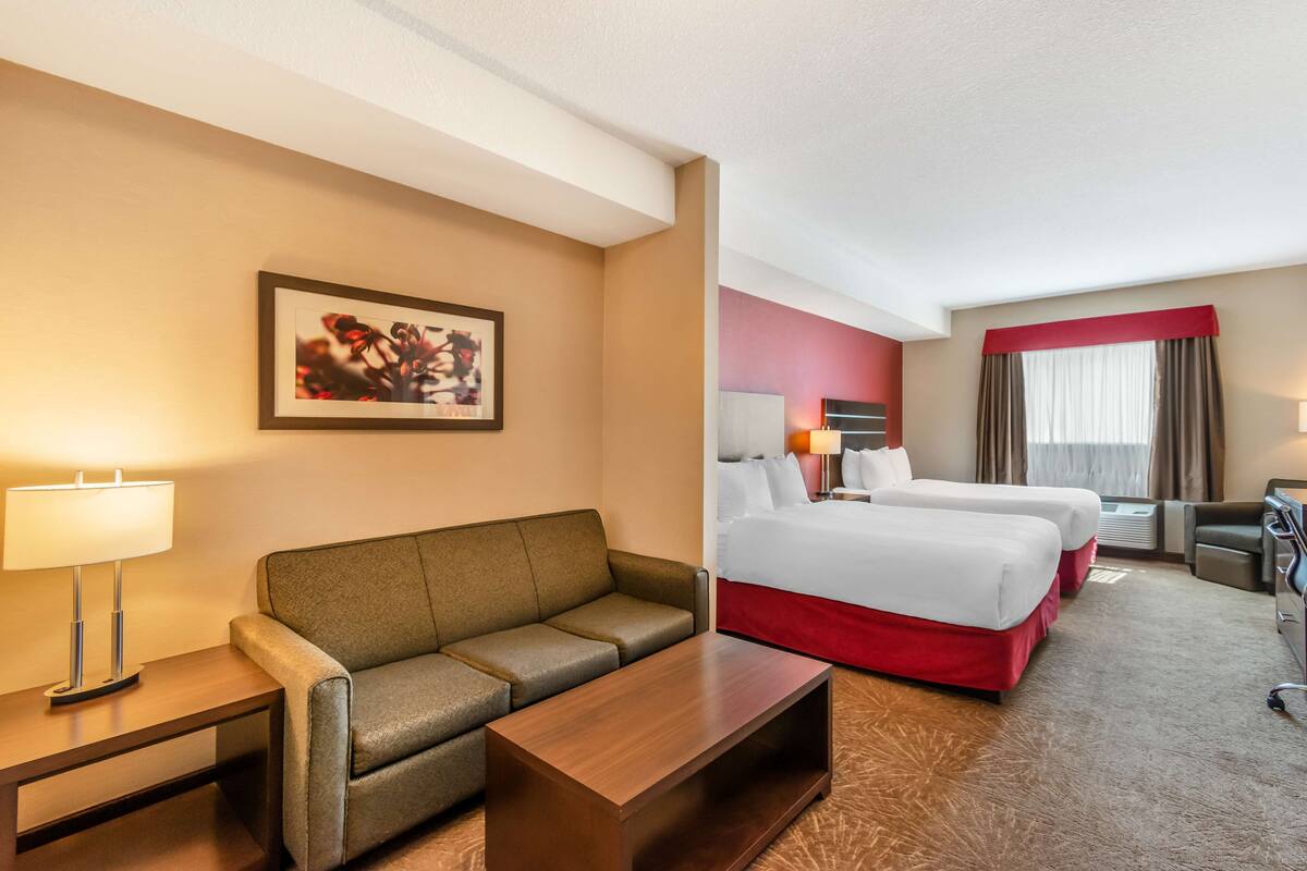 Een hotelkamer met een bank, twee bedden, een bureau en een lamp.
