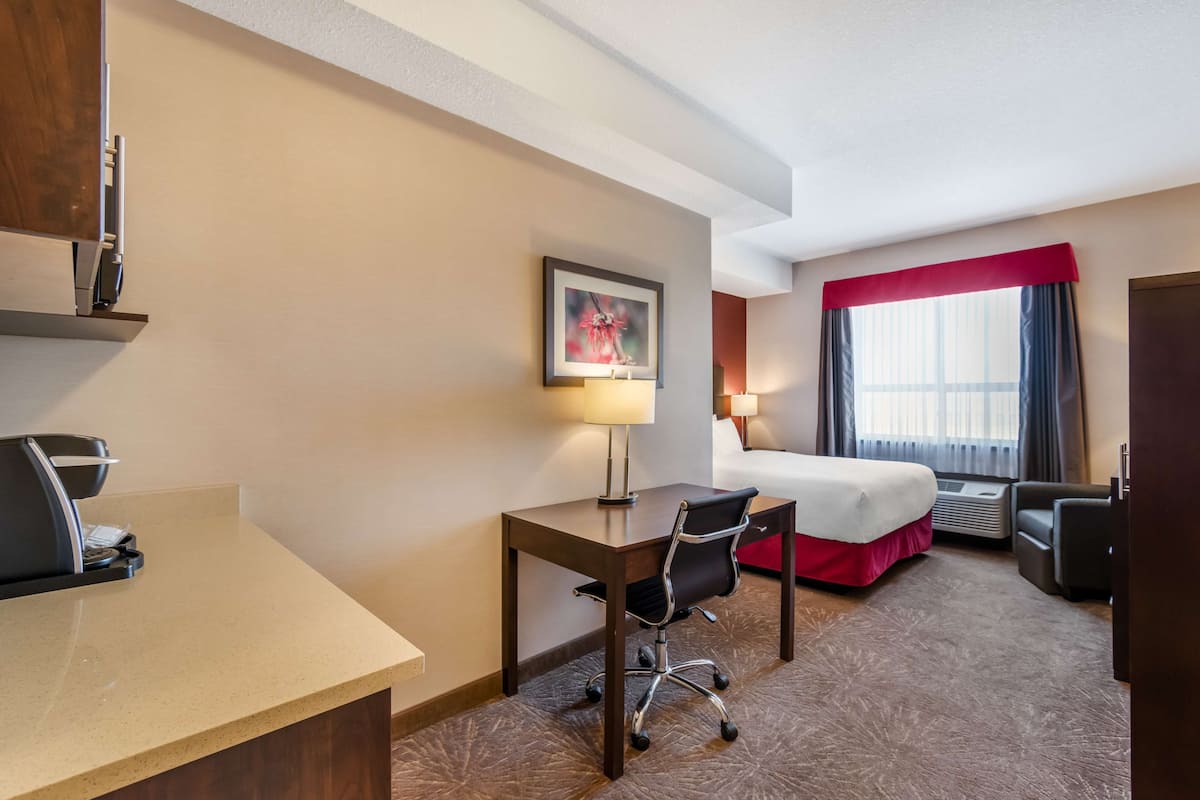 Een hotelkamer met een bed, bureau, stoel, twee lampen en een raam met gordijnen.