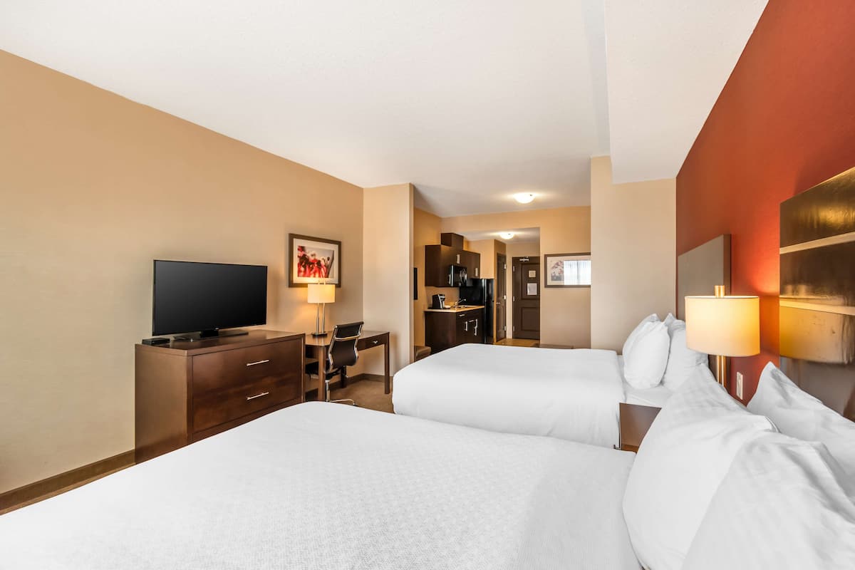 Een hotelkamer met twee bedden, een bureau met stoel, een televisie en een kitchenette.