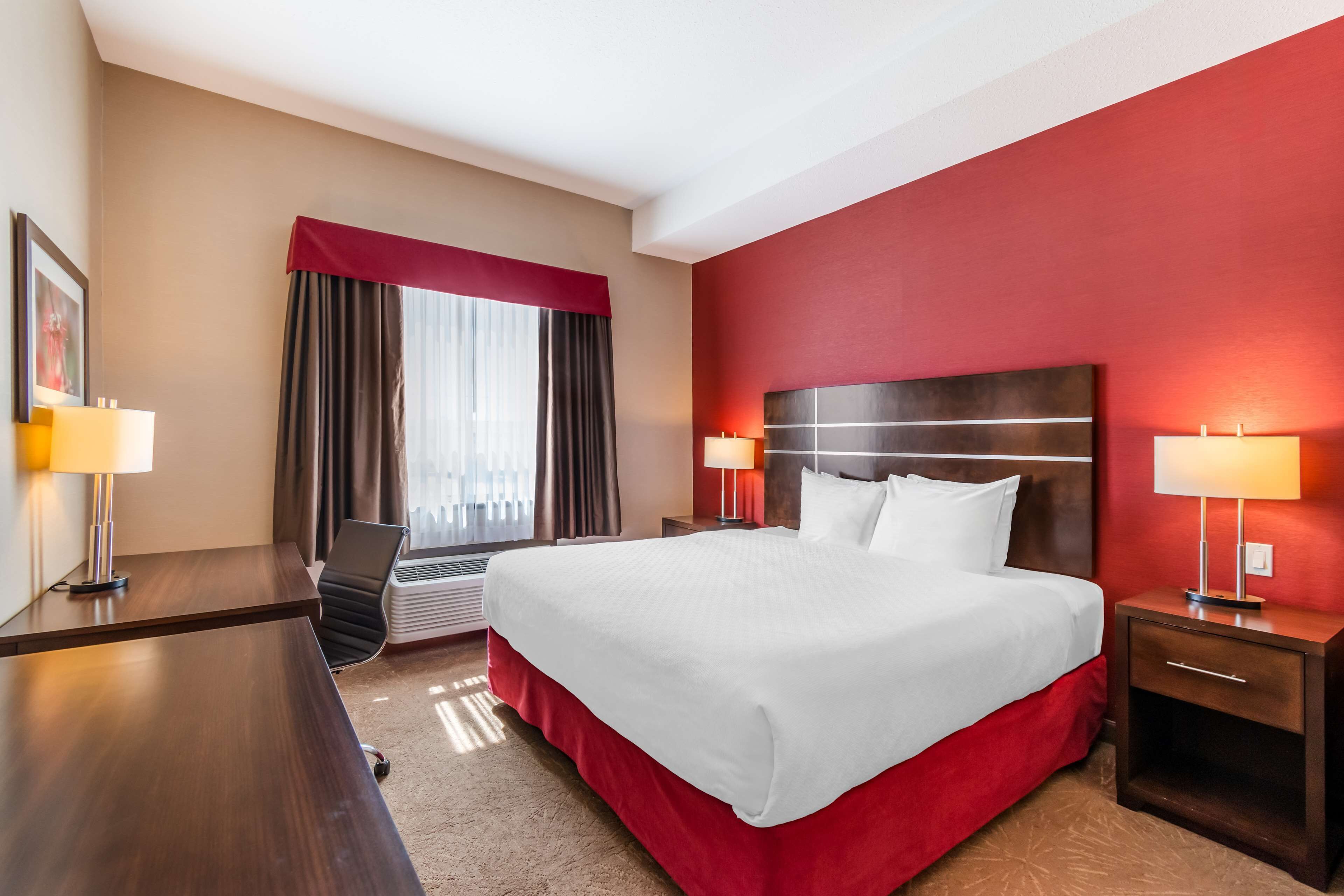 Habitación de hotel con una cama grande, un escritorio y una silla. Se ve una ventana con cortinas y vistas a la ciudad.