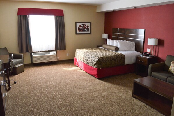 A hotel room with a large bed, a desk, a chair, a lamp, and an air conditioning unit. - Best Western Plus Kindersley Hotel (Kindersley)