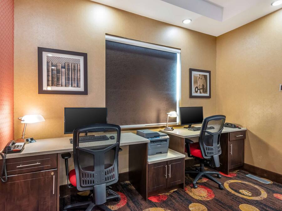 Habitación de hotel con dos escritorios, dos sillas, un teléfono, una impresora y una ventana con persianas.