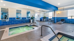 A modern indoor pool area with blue and white walls, a seating area with tables and chairs, and a visible hot tub. - Best Western Plus Kindersley Hotel (Kindersley)