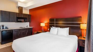A hotel room with a large bed, a microwave, a coffee maker, and a nightstand with a lamp.