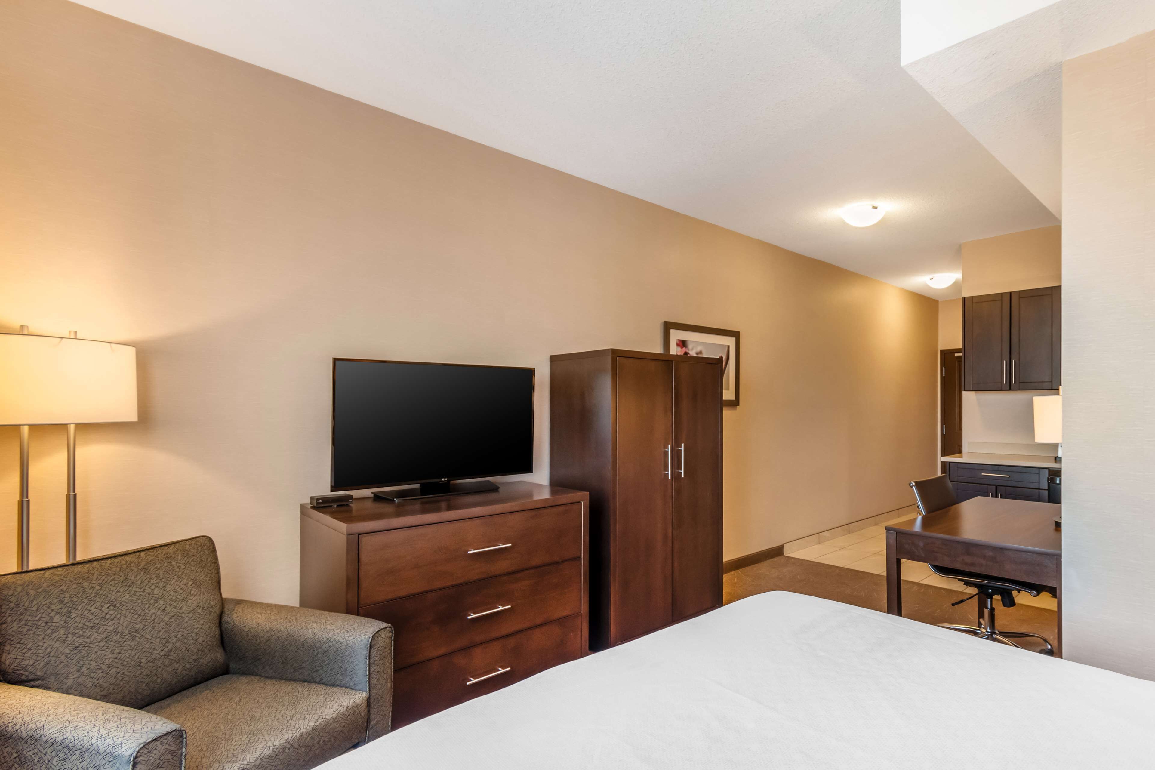 Ein Hotelzimmer mit einem Bett, einem Fernseher auf einer Holzkommode, einem Schreibtisch mit Stuhl und einem Kleiderschrank.