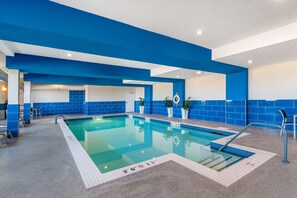 Una piscina interior con paredes de azulejos azules y blancos, agua cristalina y una silla de socorrista.