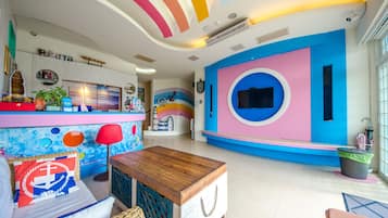 Um quarto vibrante com teto colorido, uma mesa de madeira e uma área de estar com almofada estampada.