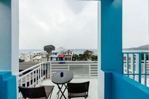 A balcony with two wicker chairs and a small table, overlooking a street with buildings and a clear sky. - Love Jane B&B (Hengchun)