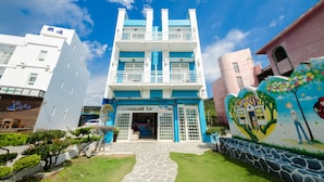 A multi-story building with a blue and white facade, a central entrance, and a mural on the right side. - Love Jane B&B (Hengchun)