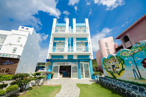 A multi-story building with a blue and white facade, a central entrance, and a mural on the right side. - Love Jane B&B (Hengchun)