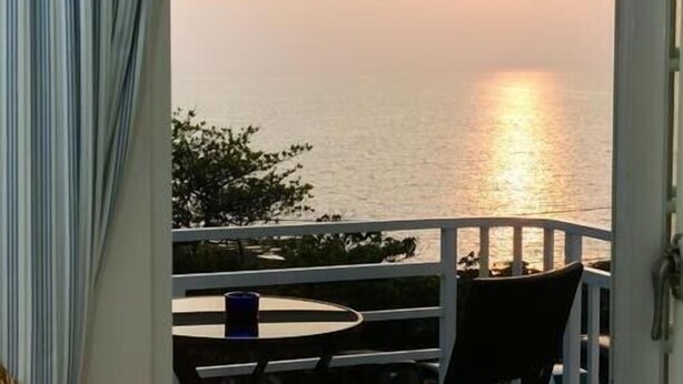A balcony with a view of the sea at sunset, a table, and two chairs. - Love Jane B&B (Hengchun)