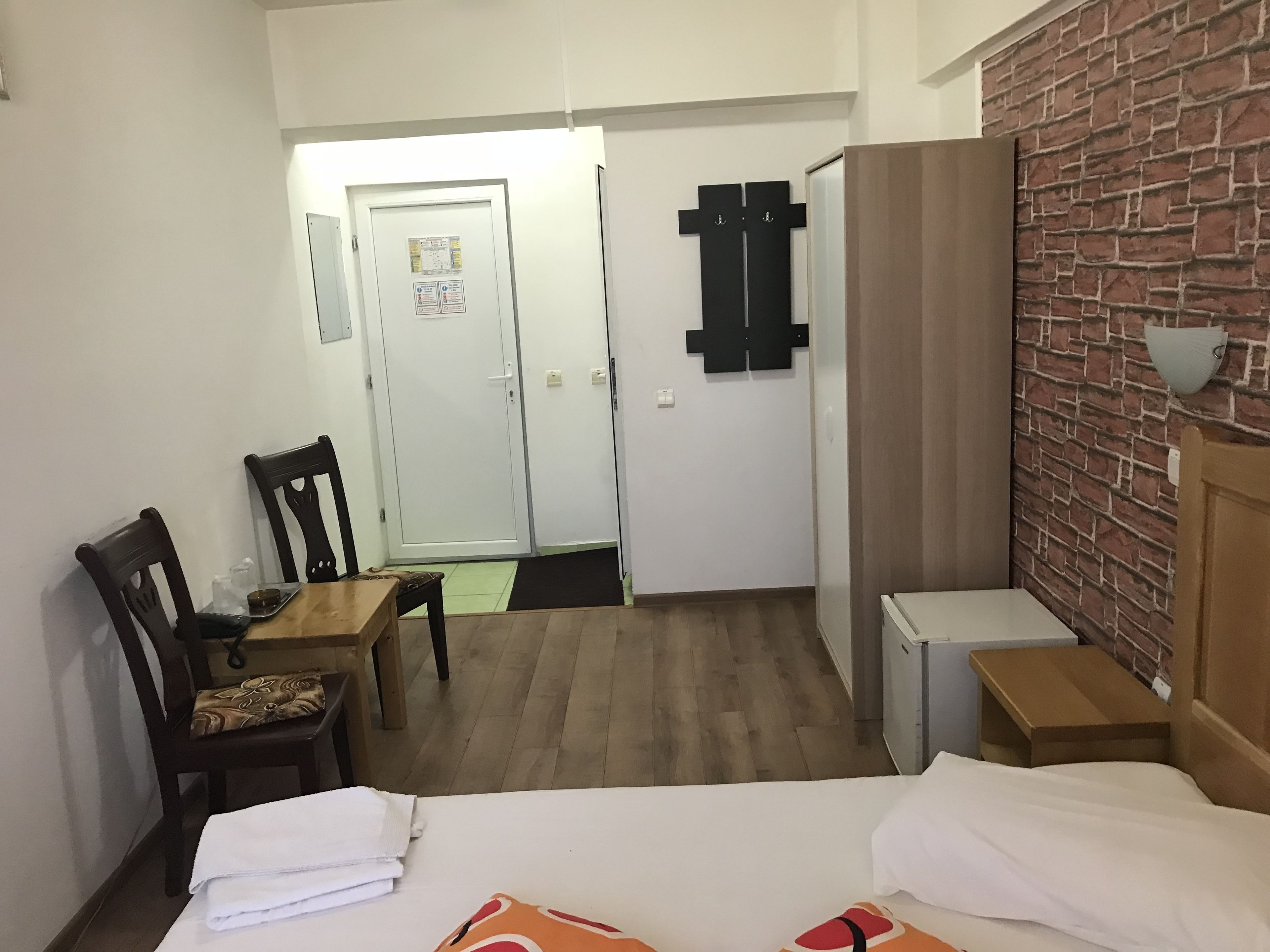 Habitació d'hotel amb un llit, escriptori, cadira, taula petita i un mur amb relleu de maó.