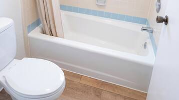Un baño con inodoro blanco, bañera con detalle de azulejos azules y suelo de madera.