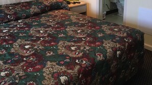 A hotel room with a large bed, a nightstand, a lamp, and a bathroom visible through an open door. - Shaws Komfort Motel (Savannah)