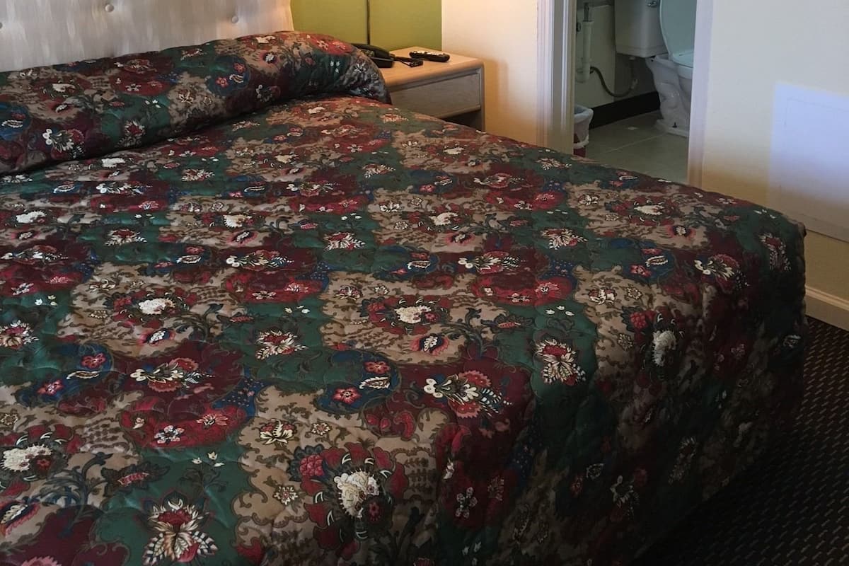 Une chambre d’hôtel avec un grand lit, une table de chevet, une lampe et une salle de bain visible à travers une porte ouverte.