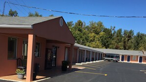 A motel with a row of rooms, a parking lot, and a clear blue sky. - Shaws Komfort Motel (Savannah)