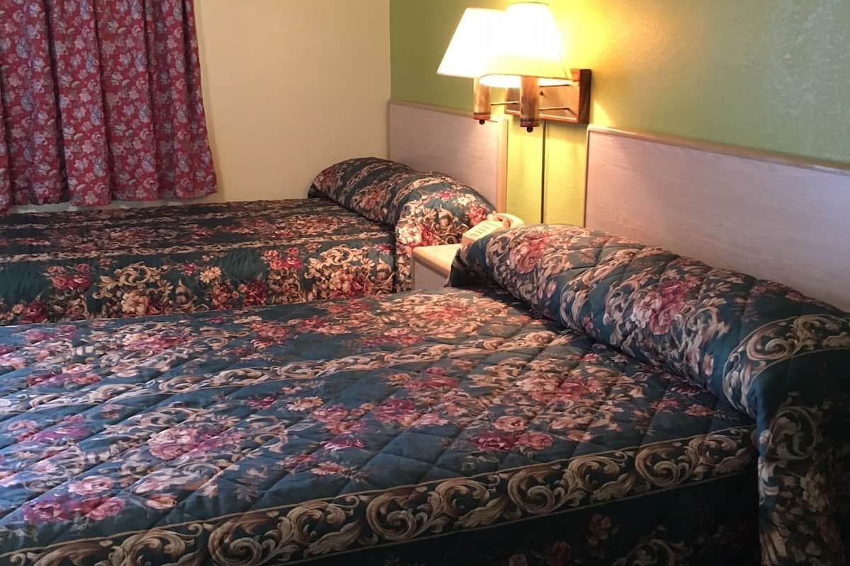 Une chambre d’hôtel avec deux lits, une literie à motifs floraux, une lampe fixée au mur et un tableau.