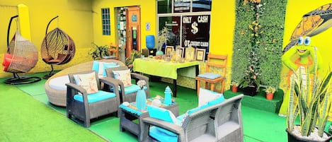 A brightly colored outdoor seating area with wicker furniture and a green floor, featuring a reception desk and a wall with a turtle mural.