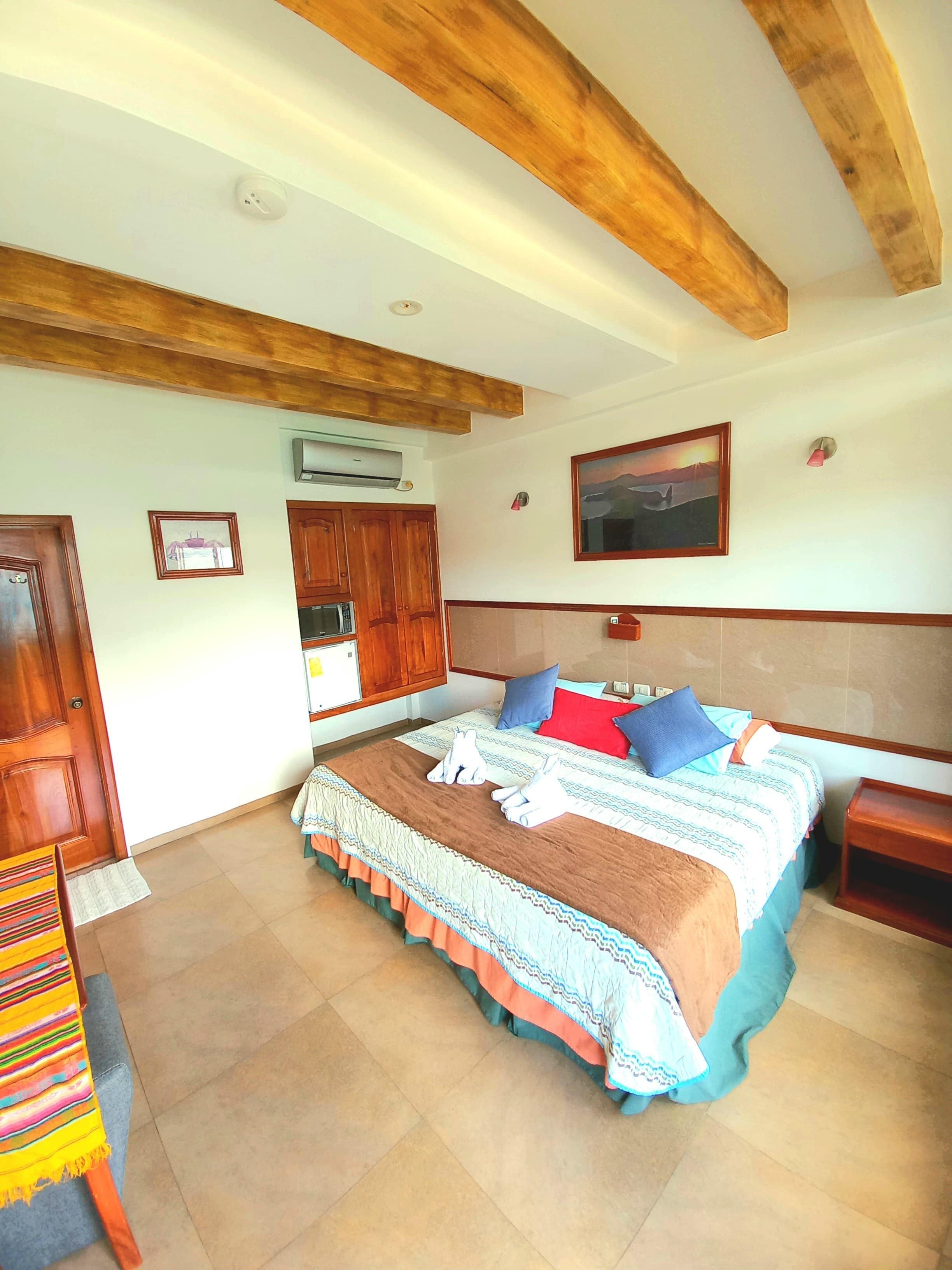 A bedroom with a large bed, wooden beams on the ceiling, an air conditioning unit, a wooden wardrobe, and a framed picture on the wall.