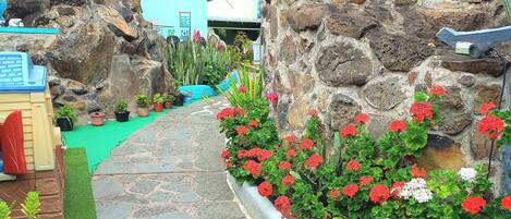 A stone pathway leading to a building with a blue exterior, surrounded by potted plants and flowers.